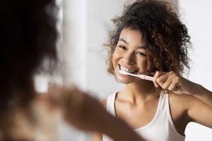 Woman looking in mirror while brushing her teeth thinking about general dentistry services