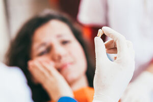 a woman holds an icepack on her cheek after dental extractions