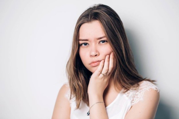 How Do I Know I Need a Dental Appointment_ a young woman holds onto the side of her mouth in pain wondering if she should make a dental appointment