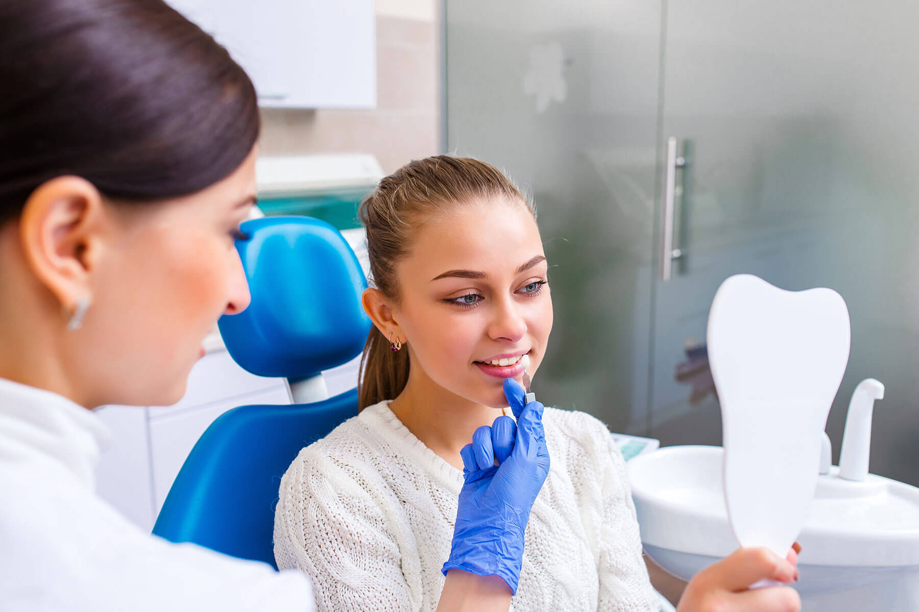 a dental professional holds her gloved hand to a patients mouth while patient receives a consultation for a cosmetic dentistry procedure