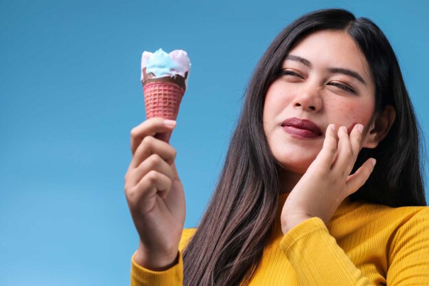 How Do I Know I Have Sensitive Teeth_ a woman holds an ice cream cone in one hand and raises her other hand to her jaw while experiencing pain in her sensitive teeth