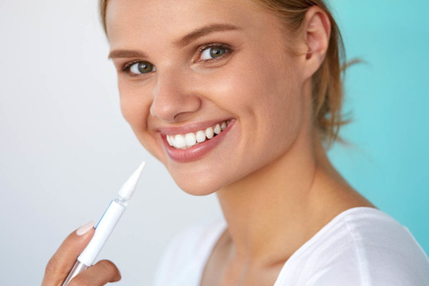 Are Teeth Whitening Pens Safe a woman smiles and holds up one of the many teeth whitening pens to her mouth