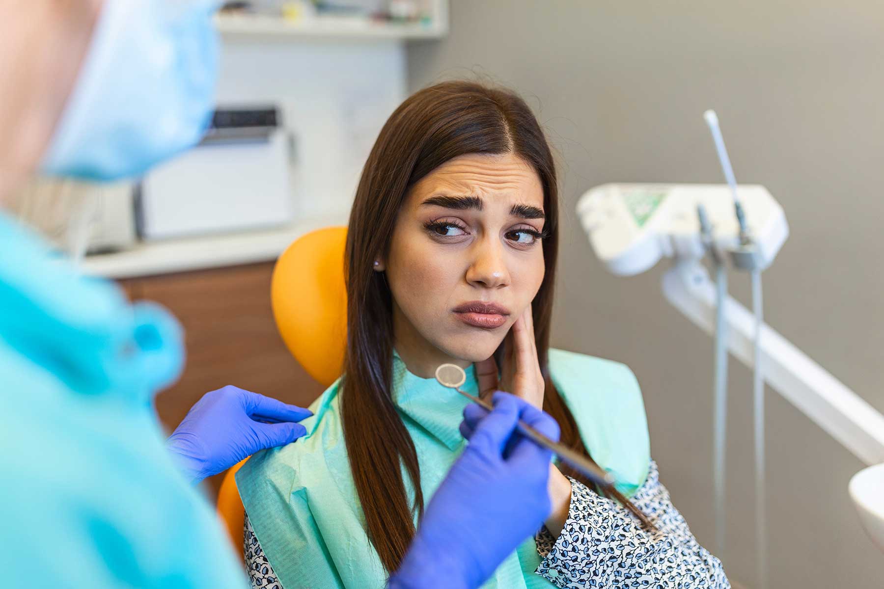 a patient sits in dental exam chair in pain while the dentist explains the root canal procedure