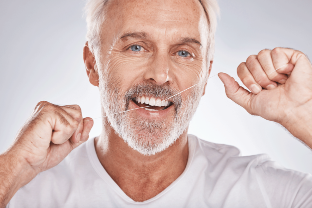 an older man with a beard flosses his teeth knowing that flossing helps achieve healthy gums