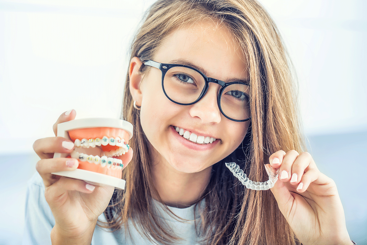 Invisalign-Clear-Aligner-Services-in-Houston-Texas a teen girl holds up her clear aligners in one hand and model of a mouth with braces on the other after receiving invisalign clear aligner services in houston texas