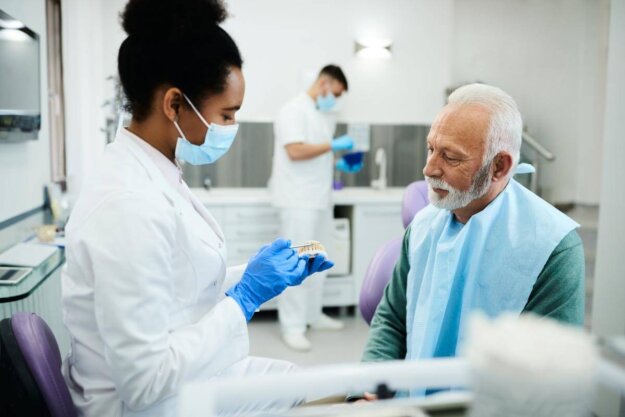 Temporary Crown Cost How Much Is It On Average_ a dental professional holds a teeth model while talking to patient about the temporary crown cost and procedure
