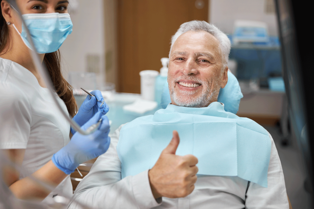 How-to-Choose-a-Dentist-in-Houston man sits in dental exam chair giving a thumbs up while dentist in houston stands next to him ready to start his procedure