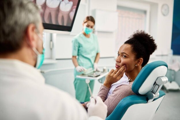 Can Crowns Get Cavities_Dental Crowns Demystified a patient sits in a dental exam chair holding the side of her face asking the dentist sitting next to her can crowns get cavities