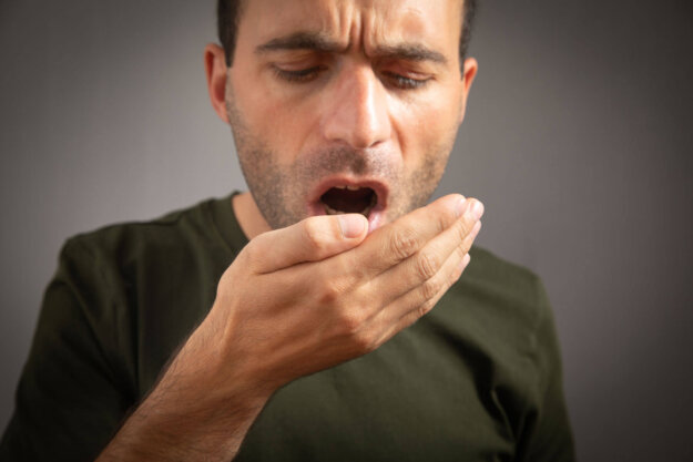 How to Get Halitosis Cured Permanently man blows into his hand wondering if halitosis can be cured permanently
