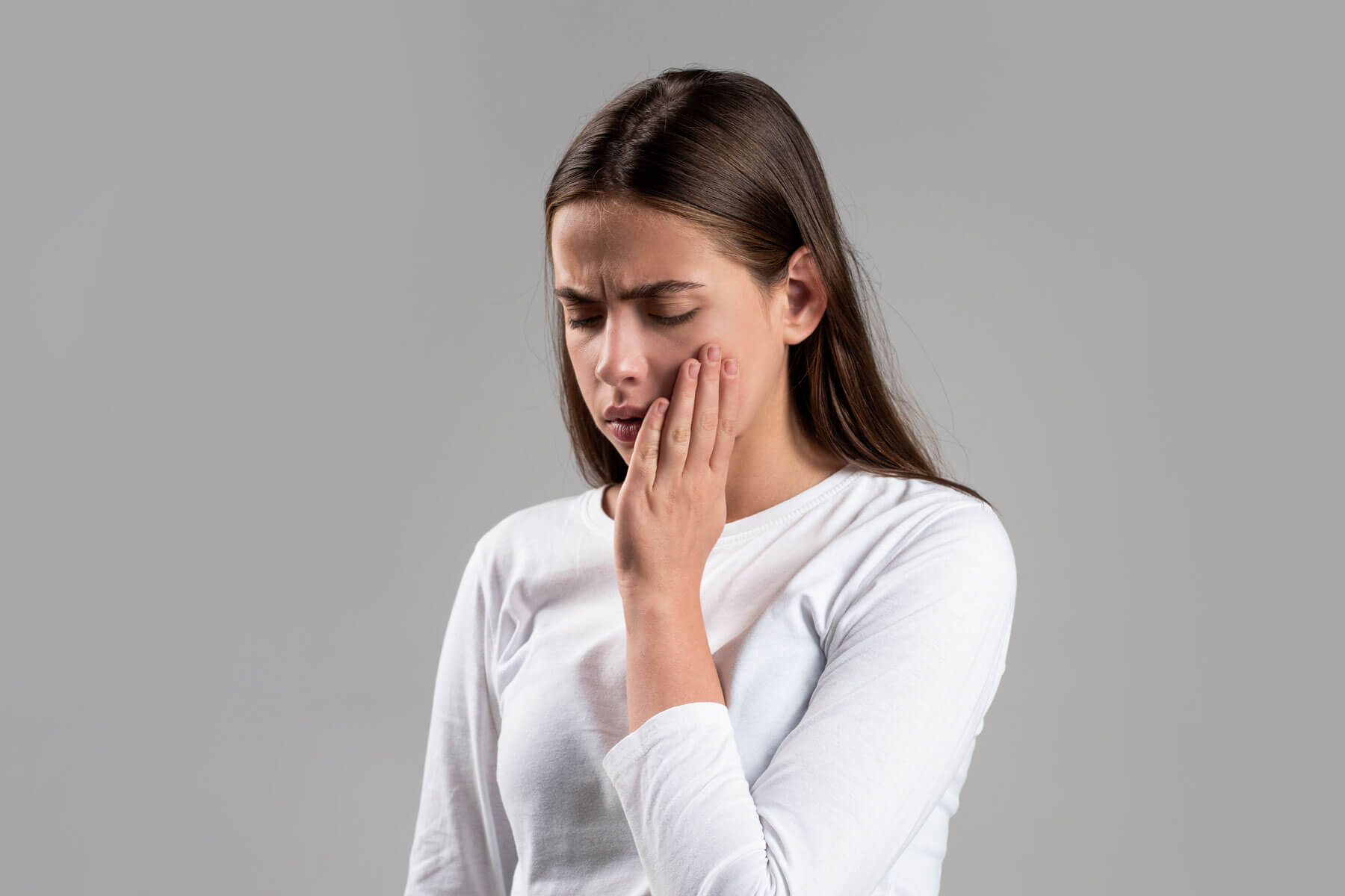 Why Do I Keep Biting My Cheek – It’s Your Teeth a woman with dark hair in a long white sleeve shirt holds the side of her mouth and wonders why do i keep biting my cheek