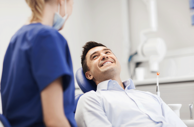 man smiles while laying back in dental exam chair while asking how long does tooth extraction take to heal to the dental professional next to him