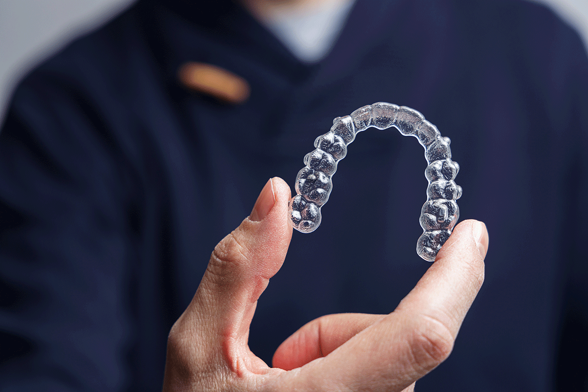 Cheapest-Clear-Aligners–Getting-the-Best-Quality-at-a-Low-Price dental professional holds a clear aligner while discussing cheapest clear aligners to a patient