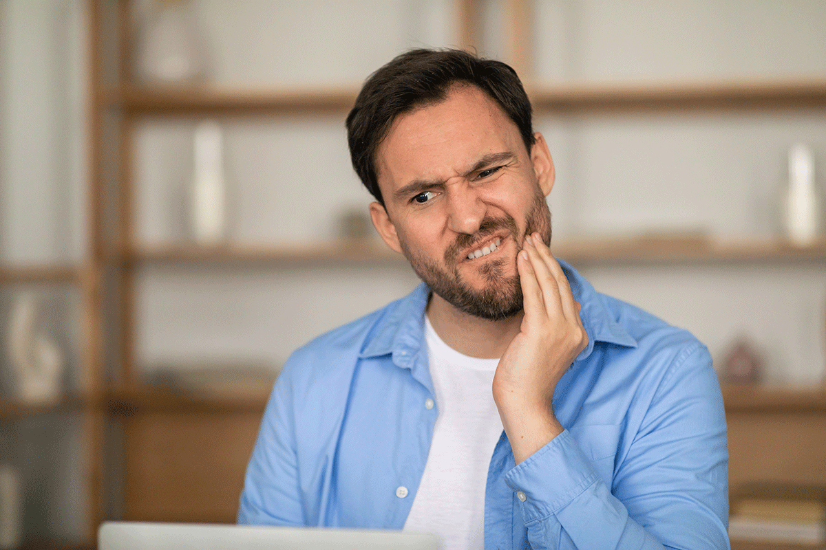How-to-Tell-if-You-Have-an-Crown-That-Doesnt-Fit man with beard appears to be in pain and holds the side of his mouth while wondering if hes experiencing bad fitting crown symptoms