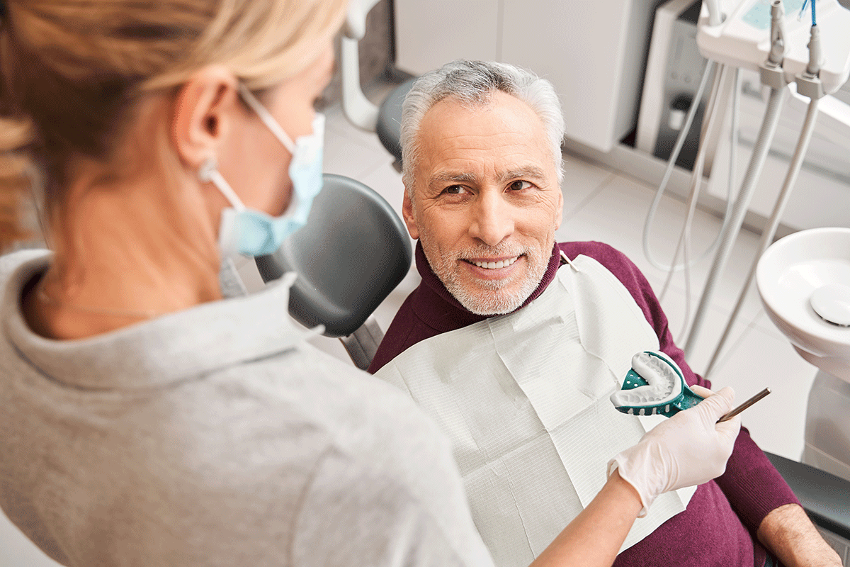 How-to-Choose-Natural-Looking-Dentures male dental patient sits in a chair while he gets molds done for natural looking dentures