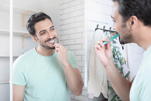 man smiling looking in a mirror and brushing his teeth