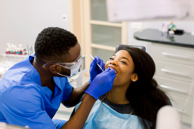 a dental expert examines a patient while explaining to her the benefits of regular dental check-ups
