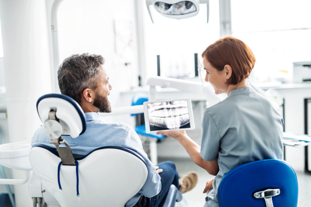 Importance-Of-Routine-Dental-Care a dental professional holds patients xrays and talks to the patient about the importance of routine dental care