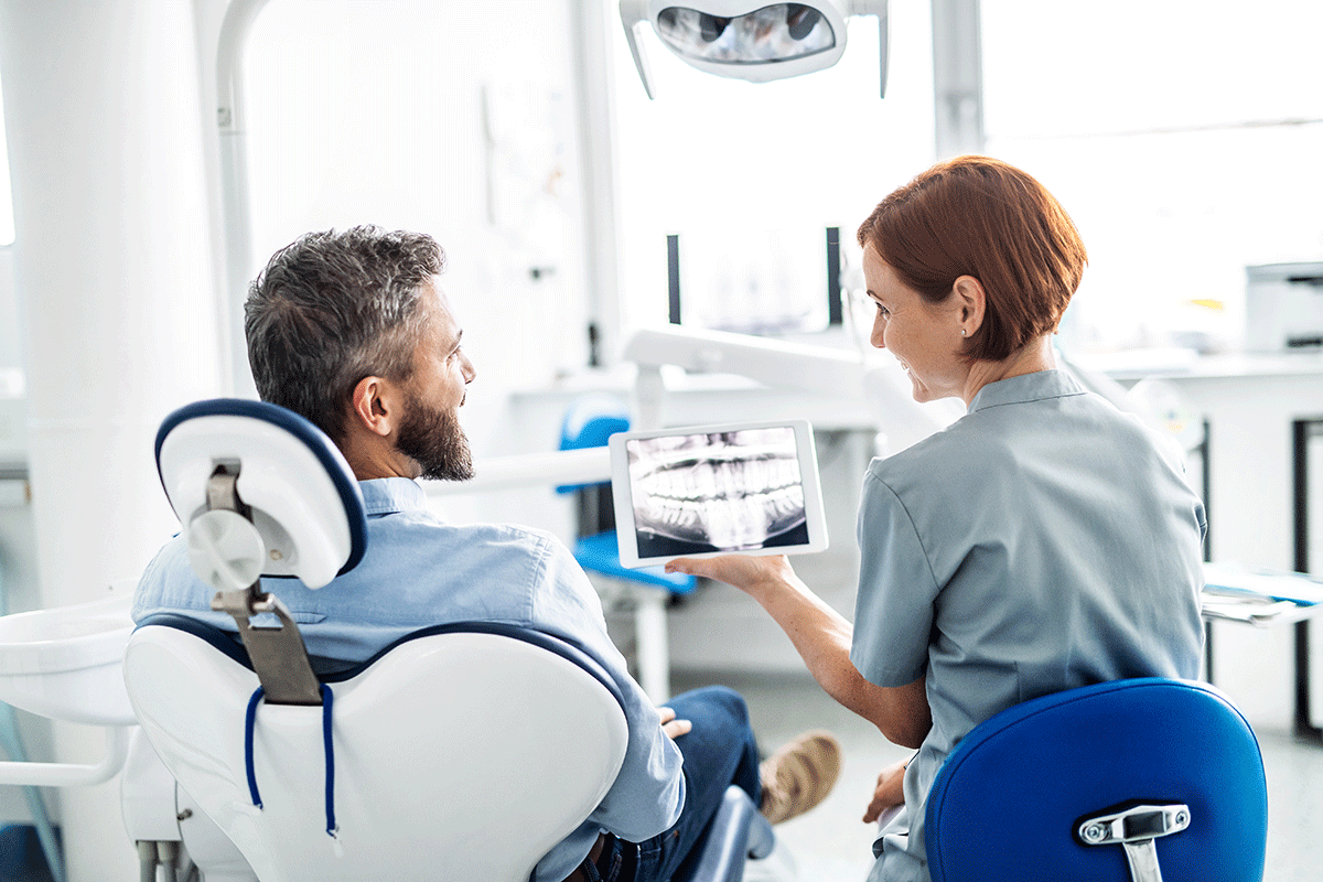 Importance-Of-Routine-Dental-Care a dental professional holds patients xrays and talks to the patient about the importance of routine dental care