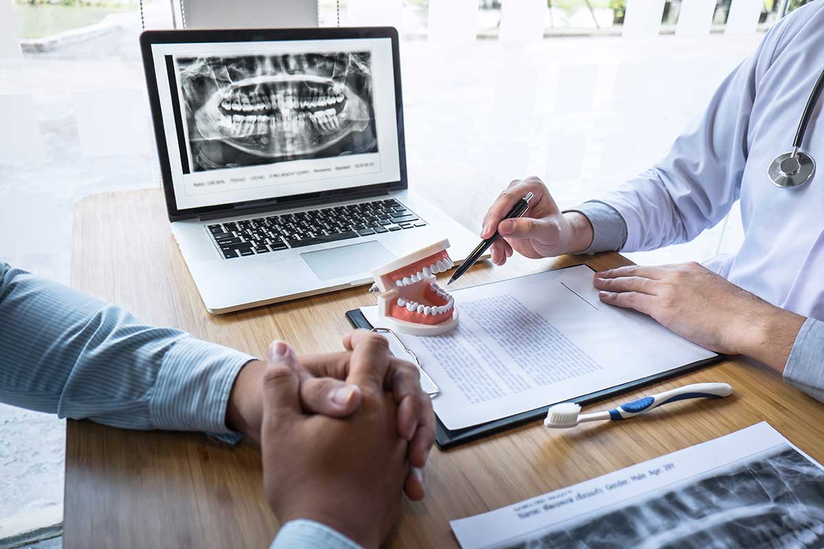 a patient sits at a desk with a dentist while the dentist is discussing what is the cost of dental implants