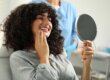 a patient sits in a dental exam chair and smiles in a mirror admiring her gum contouring and its healing
