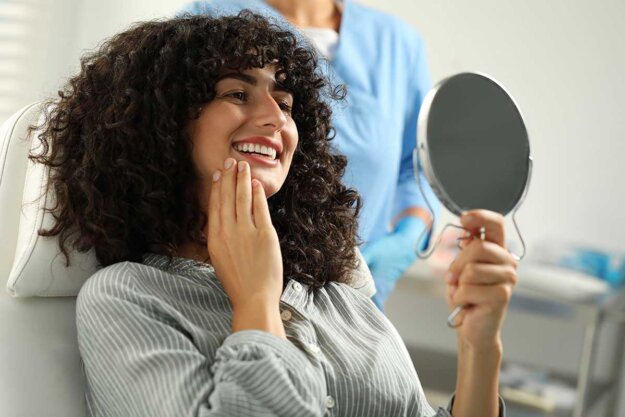 a patient sits in a dental exam chair and smiles in a mirror admiring her gum contouring and its healing