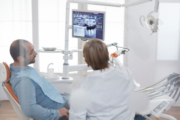 The Pros and Cons of Dental Implants- Is It Right for Your Smile a dentist sits with a patient in an exam room explaining to him the pro and cons of dental implants