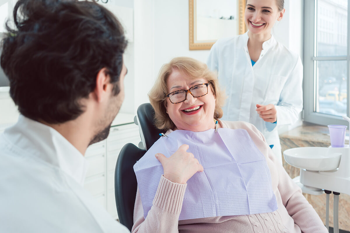 woman with glasses is sitting in dental exam chair and asks the two dental professionals around her what is composite bonding