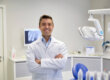a smiling dentist stands in exam room after telling a patient about the signs they need to see an emergency dentist