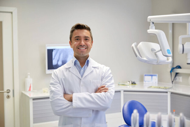 5 Signs You Need to See an Emergency Dentist a smiling dentist stands in exam room after telling a patient about the signs they need to see an emergency dentist