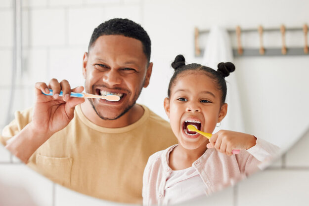 How To Prevent Cavities a dad and his daughter brush their teeth after learning how to prevent cavities while looking at their reflections in a mirror