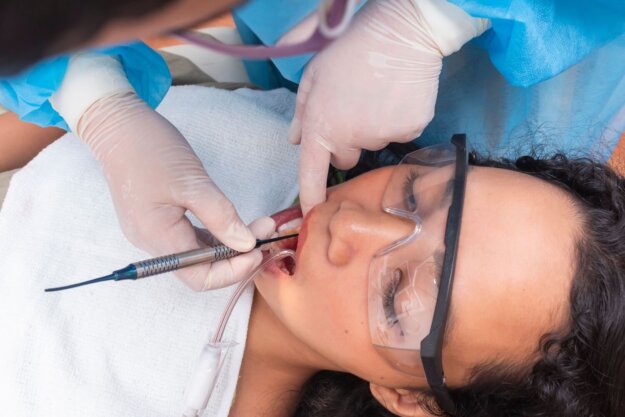 Crowns vs Fillings Overhead view of a dental procedure, showing a patient wearing protective goggles while a dentist in gloves uses tools inside the patient’s mouth.